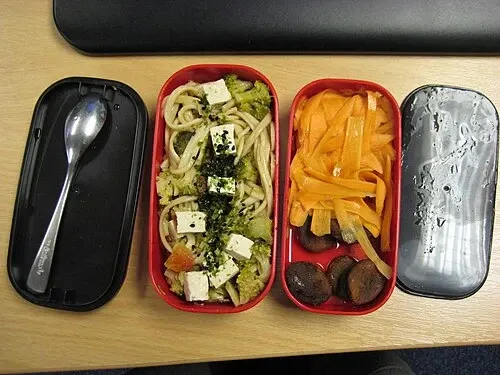 Två långsmala bentodelar med mat och avtagna lock bredvid.