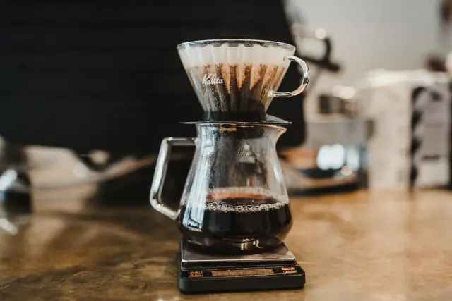 V60-handbryggare och glaskanna står på en digital våg under bryggning.
