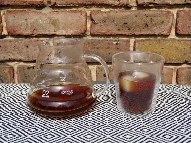 Glaskanna med kaffe bredvid ett glas med iskaffe och stora isbitar.