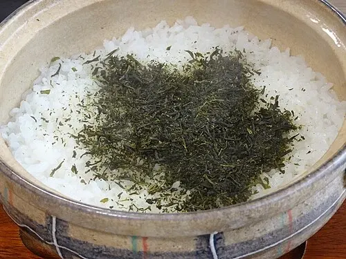 Kokt ris med gröna teblad i en japansk lergryta.