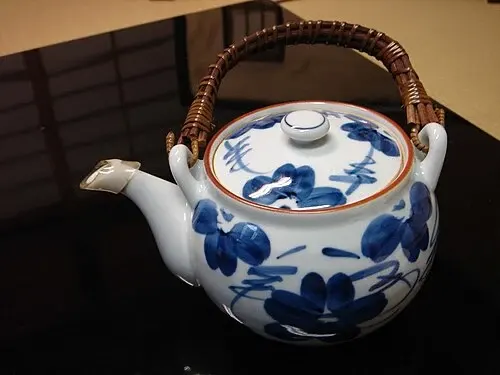 Japansk tekanna med blå dekor, lock och flätat bygelhandtag.