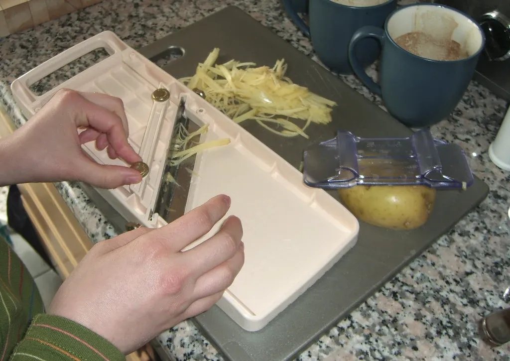 Benriner-mandolin, strimlad potatis och en skalare på en köksbänk.