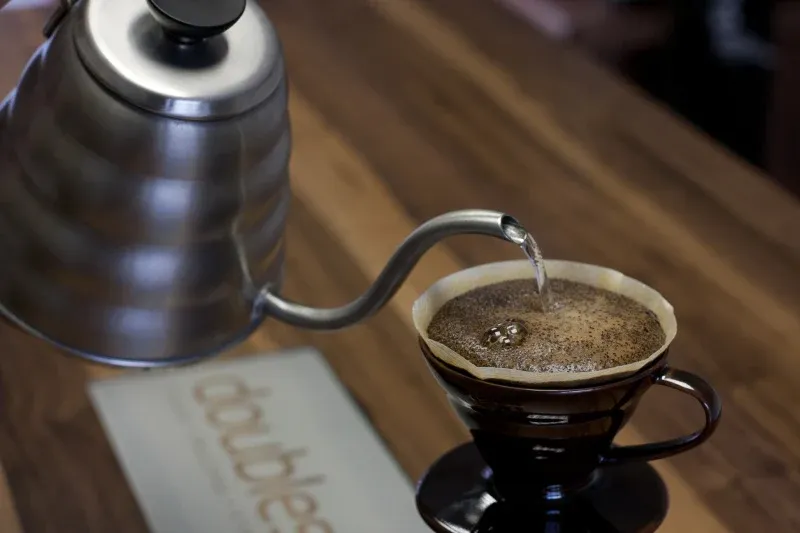 Vatten hälls från en svanhalskanna i en handbryggare med kaffe och pappersfilter.