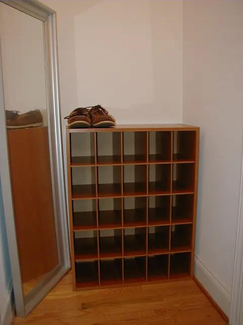En smal träskohylla med separata fack står intill en dörr och en spegel.