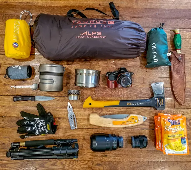Friluftsutrustning med kokkärl, flaska och redskap utlagd före packning