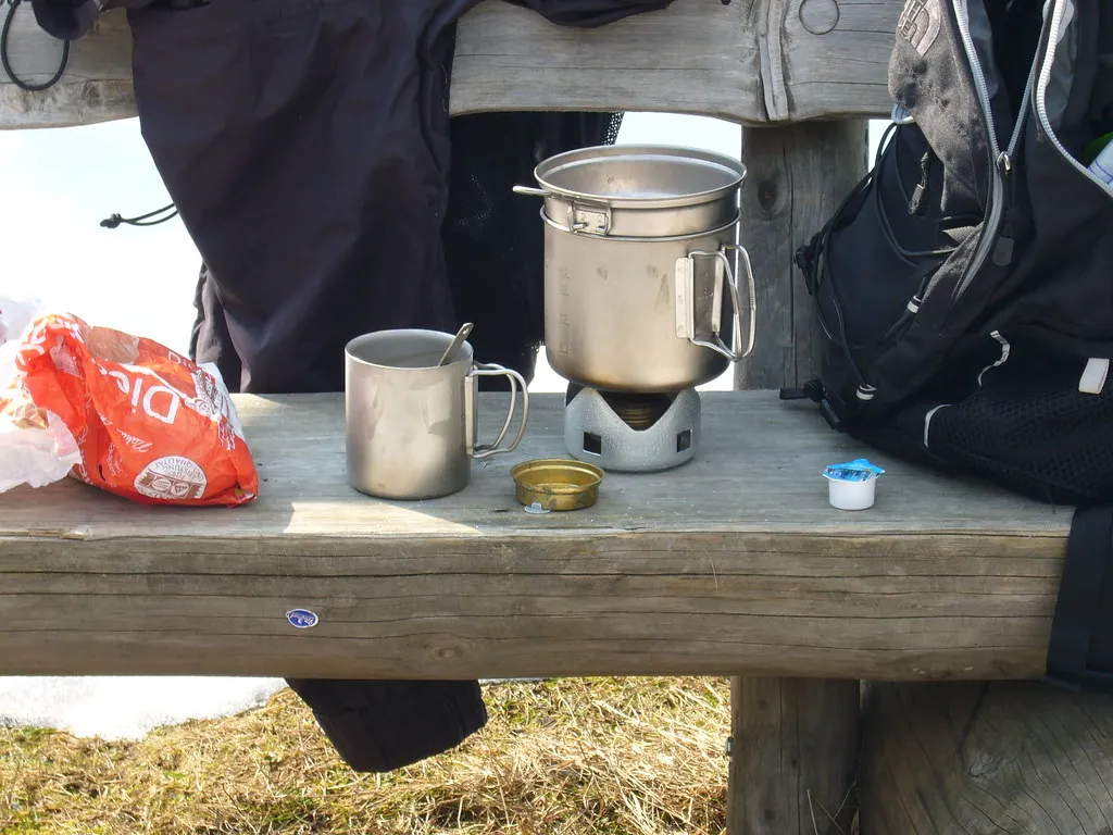 Metallmugg och kokkärl på ett träbord under en friluftstur
