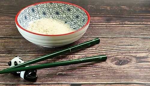 Grüne Essstäbchen auf einer Panda-Ablage neben einer Reisschale.