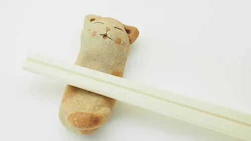 Eine katzenförmige Stäbchenablage trägt ein Paar helle Essstäbchen.