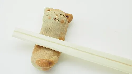 Eine katzenförmige Stäbchenablage trägt ein Paar helle Essstäbchen.