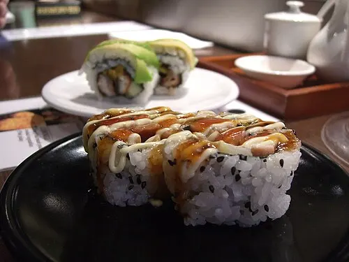 Sushi auf einem kleinen schwarzen Teller, dahinter ein weiterer heller Teller.