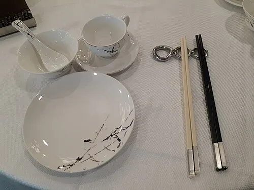 Gedeck mit hellen Tellern, Tasse, Löffel und unterschiedlichen Essstäbchen in einem chinesischen Restaurant.