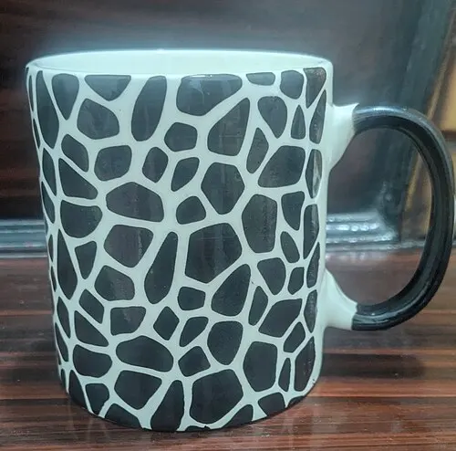 Hoher Keramikbecher mit dunklem Henkel und geometrischem Muster.