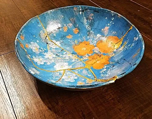 Keramikschale mit goldfarben hervorgehobenen Reparaturlinien, von der Quelle als Kintsugi beschrieben.