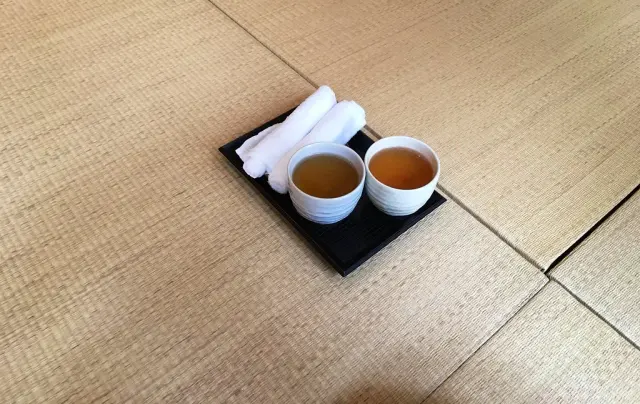 Zwei weiße Teebecher und gerollte Tücher auf einem schwarzen Tablett auf Tatami.