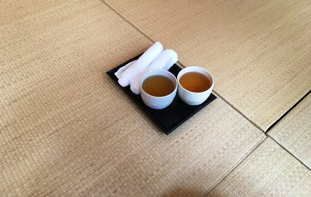 Zwei weiße Teebecher und gerollte Tücher auf einem schwarzen Tablett auf Tatami.