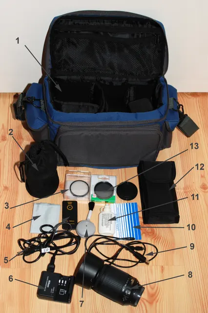 Geöffnete Fototasche neben Objektiv, Filtern, Reinigungszubehör und Kabeln