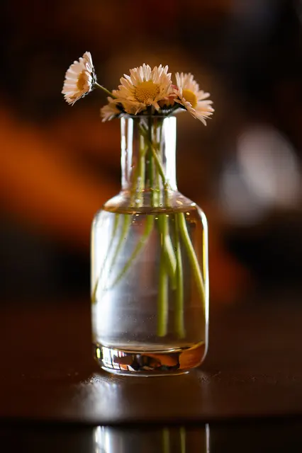 Kleine Blumenvase mit Blüten vor einem unscharfen warmen Hintergrund