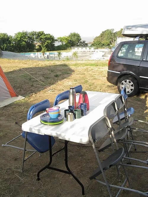 Campingtisch mit mehreren Bechern und Frühstückszubehör zwischen Klappstühlen