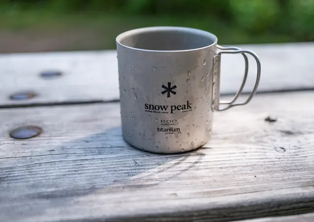 Doppelwandiger Snow-Peak-Titanbecher mit Klapphenkel auf einem Holztisch
