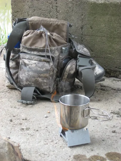 Kleines Metall-Kochgefäß auf einem Esbit-Kocher vor einem Rucksack