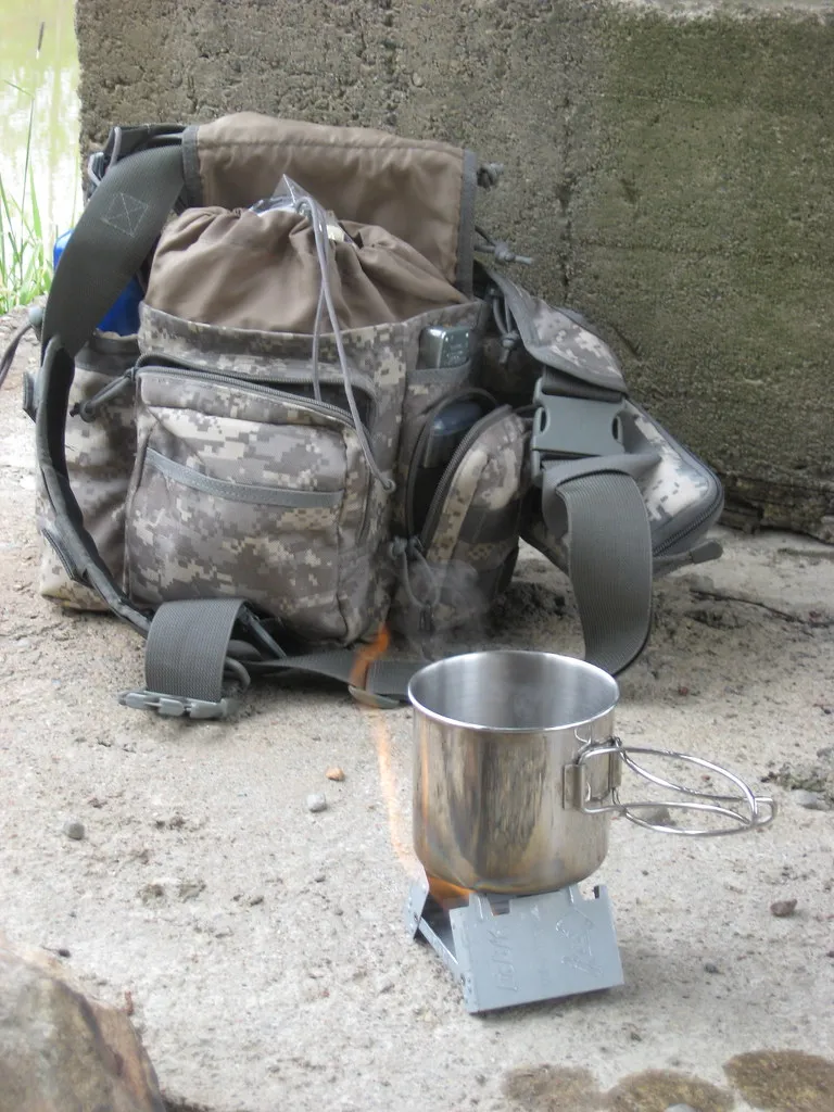 Kleines Metall-Kochgefäß auf einem Esbit-Kocher vor einem Rucksack