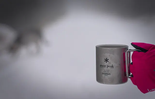 Snow-Peak-Titanbecher mit Henkel neben einem farbigen Textilteil