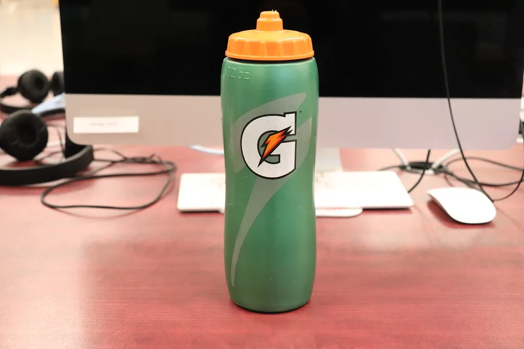 Grüne Sport-Trinkflasche mit schmalerem Fuß und orangefarbenem Verschluss