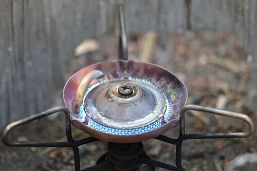 Brennender Campingkocher mit blauem Flammenring und seitlichen Topfträgern