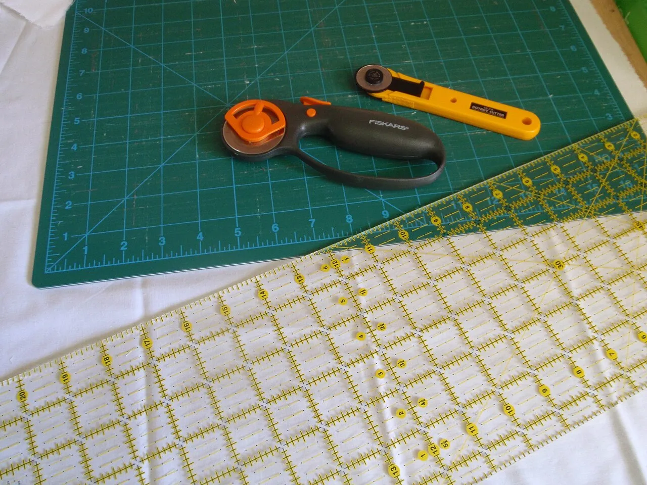 Zwei Rollschneider, transparentes Lineal und gerasterte Schneidmatte.