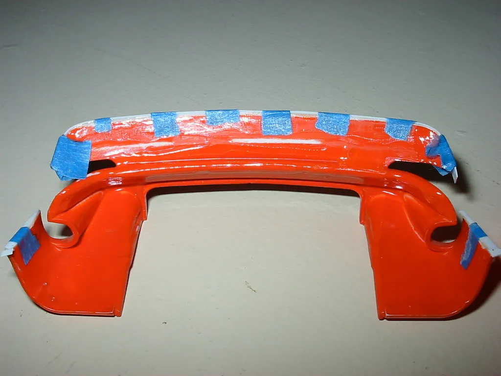 Rote Modellkarosserie mit durch Klebeband fixierten Ergänzungen bei einer Klebearbeit.
