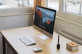 Monitorfuß, Tastatur und Maus auf einem schmalen Schreibtisch.
