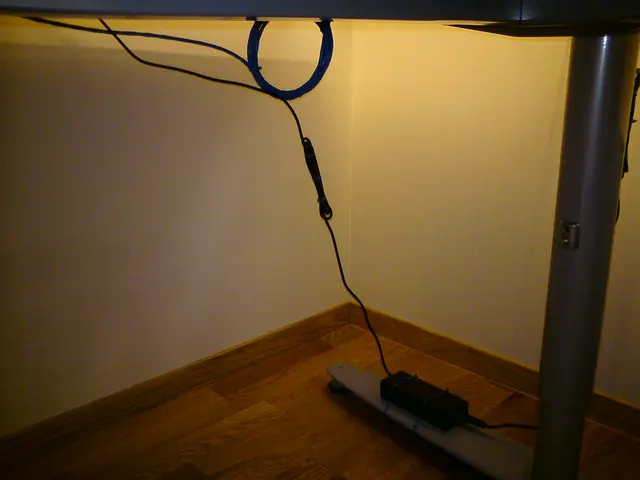 Kabel werden unter einer Tischplatte geführt, während ein Anschluss frei zur Steckdosenleiste läuft.