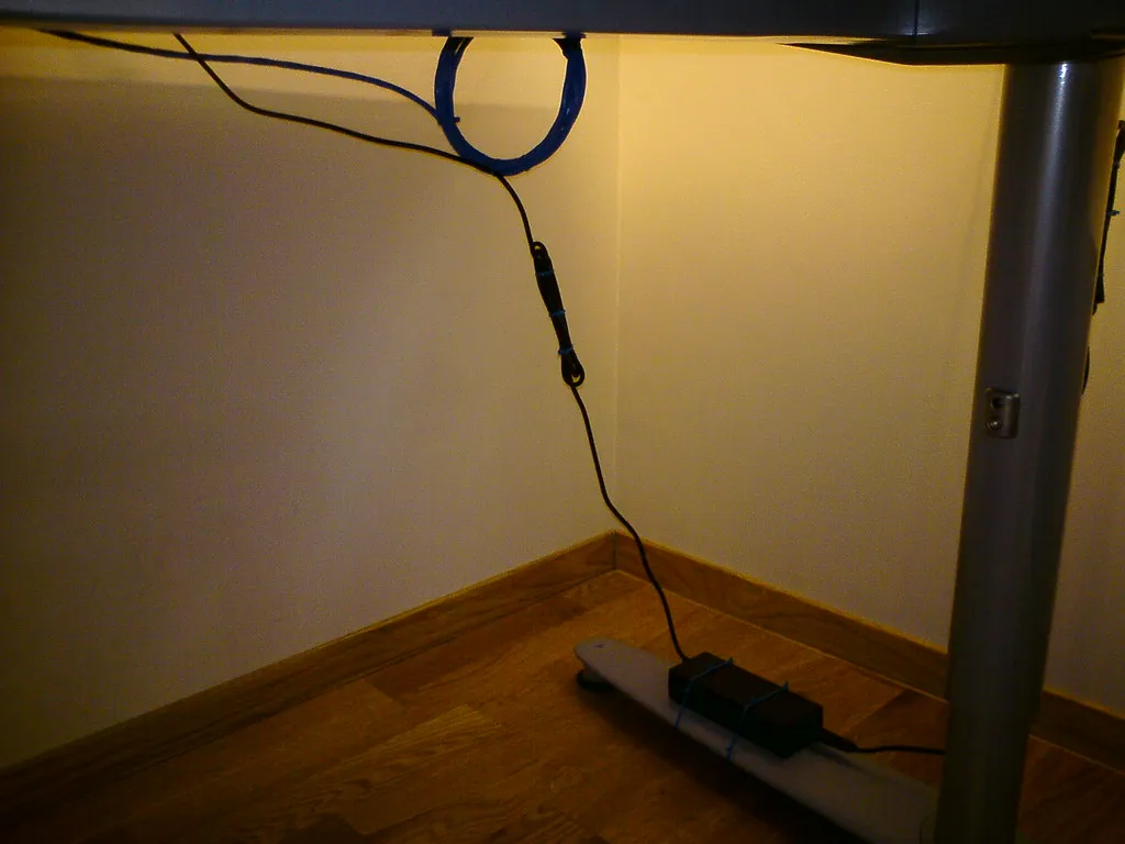 Kabel werden unter einer Tischplatte geführt, während ein Anschluss frei zur Steckdosenleiste läuft.